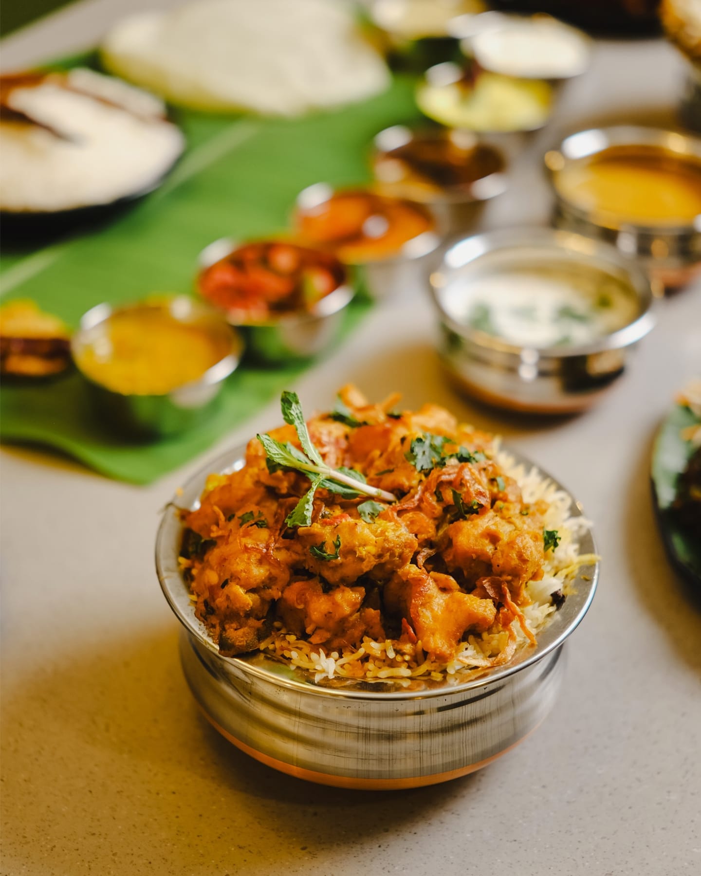 Biryani in a steel handi, with an Andhra meal on a banana leaf behind it, at Telugu Vilas